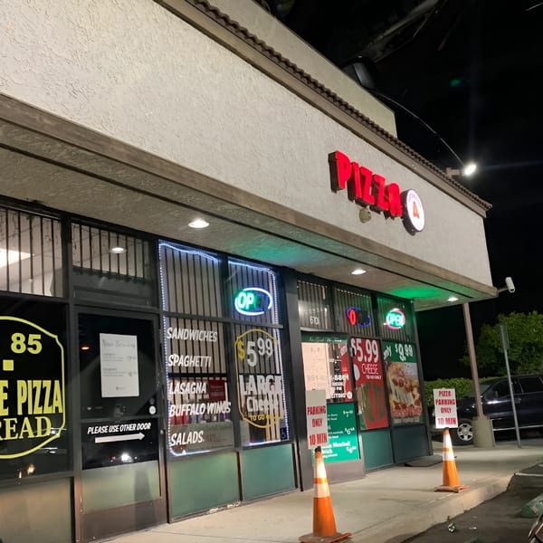 Antonious N&W Pizza storefront at night, with neon signs and menu items displayed in windows.